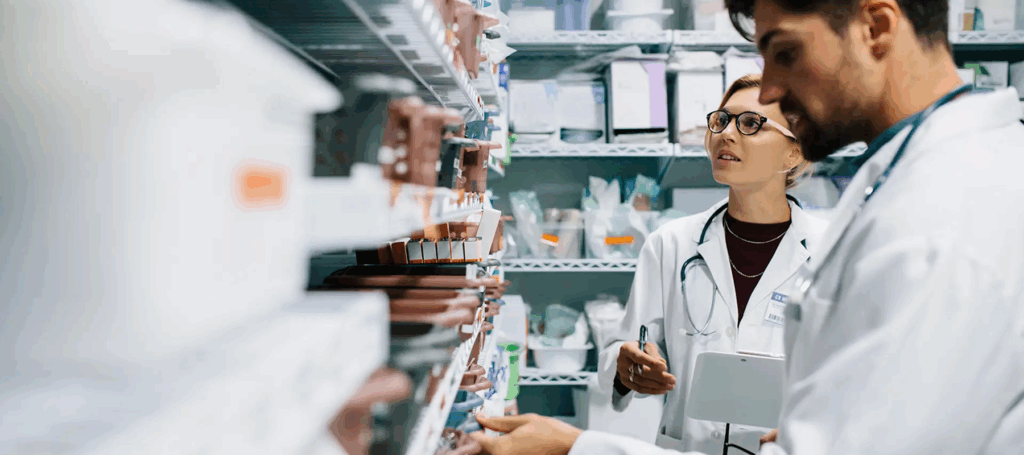 Two doctors in lab coats reviewing medical supplies on shelves inside a dispensary or pharmacy setting
